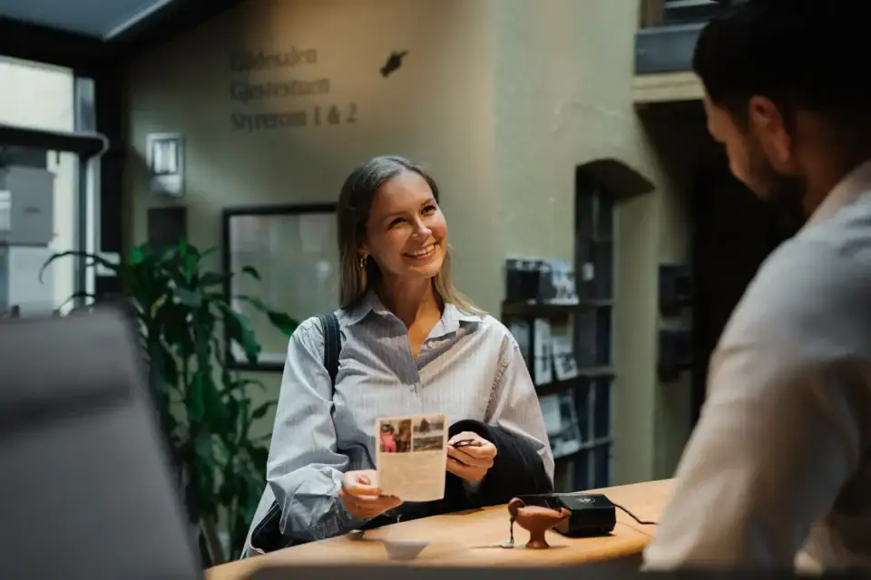 Friendly woman at Gamla Værket reception smiling and holding a brochure.